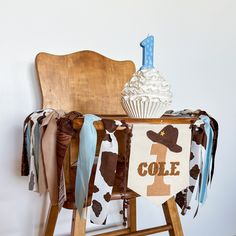 a wooden chair with a cow print banner and cupcake on it