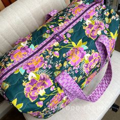 a large floral bag sitting on top of a chair next to a white chair with a purple and green flowered purse