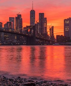 the city skyline is lit up at sunset over the water with rocks in front of it