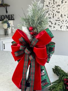 a small christmas tree with red and green bows on it's head, sitting in front of a white table