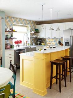 a kitchen with yellow cabinets and white counter tops, along with two stools in front of the island