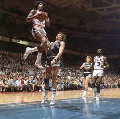 a basketball player jumping up to dunk the ball in front of two other players