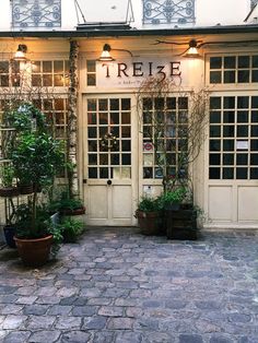 there are many potted plants in front of the storefronts on this cobblestone street