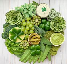 a platter filled with green vegetables and dips on top of white wooden boards