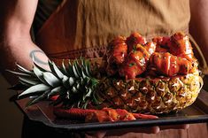 a person holding a tray with pineapples and other food items on it,