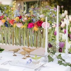 two birds are standing on the table with flowers and candles in front of them,