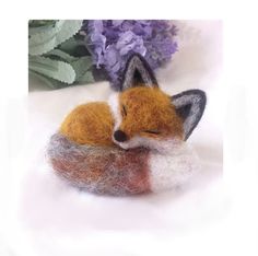 a needled fox laying on top of a piece of felt next to purple flowers