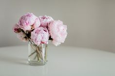 a glass vase filled with pink flowers on top of a white table next to a wall