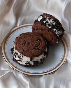 two cookies and ice cream sandwiches are on a plate with white fabric behind them,