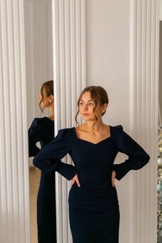 a woman standing in front of a mirror with her hands on her hips wearing a black dress