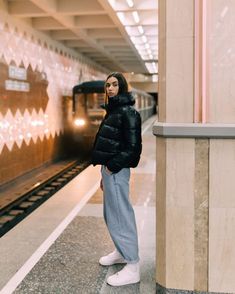 a woman standing in front of a train at a subway station with her hand on her hip