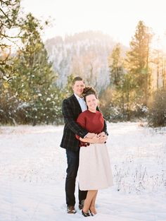 a man and woman standing in the snow with their arms around each other, smiling