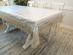 the table is covered with white lace and sits on an area rug in front of a window