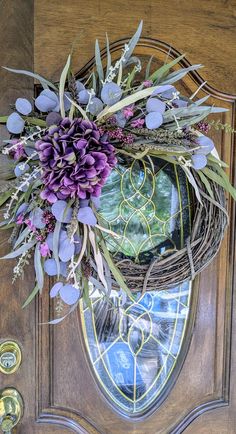 a wreath with purple flowers hanging on the front door