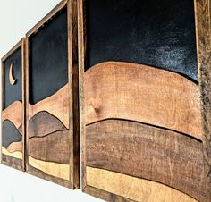 two wooden paintings hanging on the wall with black and brown paint, one is made out of wood