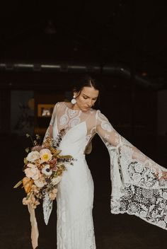 a woman in a white wedding dress holding a lace shawl over her shoulder with flowers on it