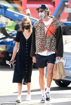 a man and woman walking down the street wearing masks