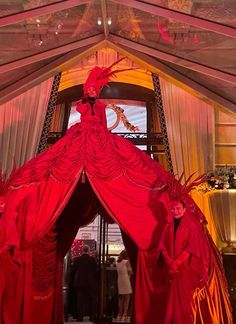 two women dressed in red are standing inside a tent with drapes on the ceiling