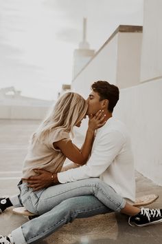 a man and woman sitting on top of a skateboard kissing in front of a building