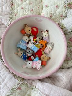 a pink bowl filled with lots of small stuffed animals on top of a quilted bed