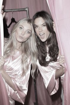 two beautiful young women standing next to each other in front of pink curtained walls