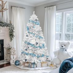 a white christmas tree with blue and silver ornaments in a living room decorated for the holidays