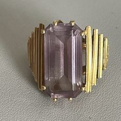 Modernist cocktail ring in yellow gold (18k) adorned with a rectangular amethyst in a claw setting supported by falling gold steps. Foreign work from the 1970s. Gross Weight: 13.66 g. Size: 53 Possibility of sizing, contact us. Further information : We issue an invoice as well as a certificate of authenticity established by our qualified gemologist (LFG Paris). Our photos are not reworked and are taken in a natural light environment. We can send you a short video upon simple request. Each piece