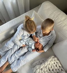 two children are laying on a white couch and one is holding the baby's head