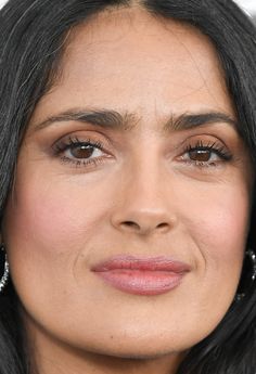 a close up of a person with long black hair and earrings on her head, looking at the camera