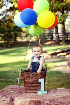 a baby sitting in a basket with balloons attached to the handle and number one on it