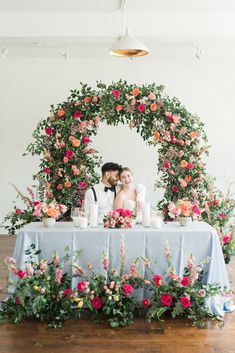 a bride and groom sitting at a table surrounded by flowers