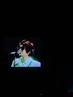 a man standing in front of a screen on top of a dark stage holding a microphone