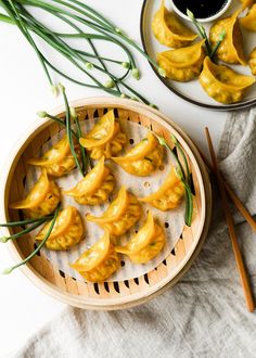 some dumplings are in a wooden bowl on a white table with chopsticks