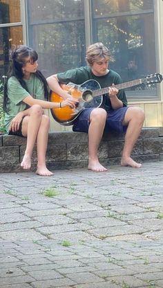 two young people sitting on a bench playing the guitar and another person standing next to them