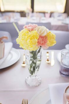 a vase filled with yellow and pink flowers sitting on top of a white table cloth