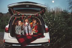 three children sitting in the back of a car with their christmas tree on the ground