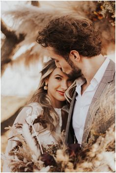 a man and woman standing next to each other in front of a tree with long hair