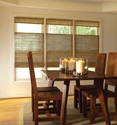 a dining room table and chairs with candles on the table in front of two windows