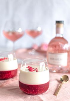 two desserts in glasses with red and white frosting on the rim, next to bottles of wine