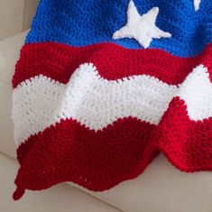 a red, white and blue crocheted blanket sitting on top of a couch