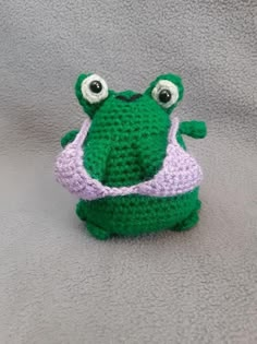 a crocheted frog hat with two eyes on it's head, sitting on a gray surface