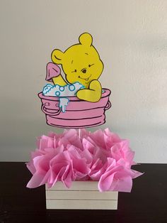 a winnie the pooh cake topper sitting in a pink cup with tissue flowers