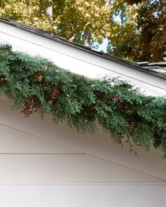 a christmas garland with pine cones and berries hanging from the side of a white house