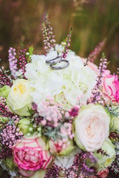 a bouquet with flowers and two wedding rings on it's top is sitting in the grass