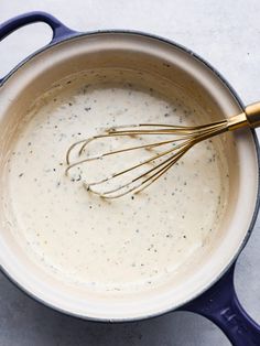 a blue pot filled with cream sauce and whisk on top of the bowl