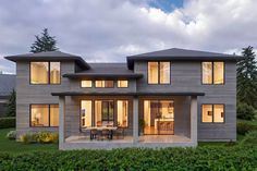 a modern house with large windows and lots of furniture in the front yard at dusk