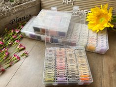 two plastic containers filled with different colored nail polishes next to some flowers and plants