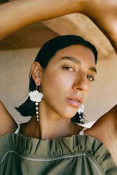 a woman wearing earrings and a green top is looking at the camera with her hands behind her head