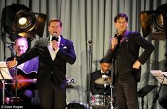 two men in tuxedos singing into microphones