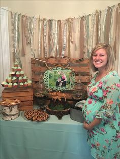 a pregnant woman standing in front of a table with cupcakes and cakes on it